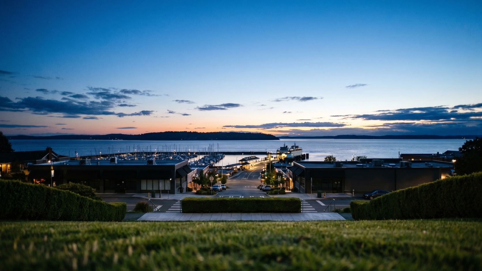 Elevated dusk view over the Edmonds Bowl with downtown rooftops sloping to the marina and Puget Sound