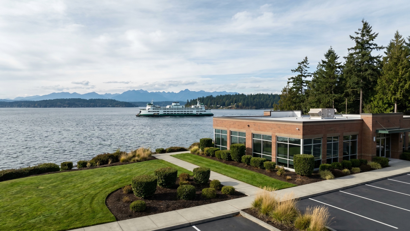 Manicured commercial property overlooking the Edmonds waterfront with a Washington State ferry crossing Puget Sound toward the Olympic Mountains at golden hour